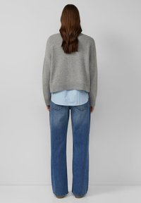 Grauer kurzer Pullover, darunter ein blau gestreiftes Hemd und locker sitzende hellblaue Jeans. Glatte Texturen; minimales Design ohne sichtbare Muster.