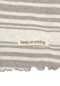 Beige- und grau gestreifter Stoff mit einer weichen Textur; zeichnet sich durch ein Etikett aus, auf dem in Schwarz auf einem cremefarbenen Hintergrund "keep on smiling" steht.
