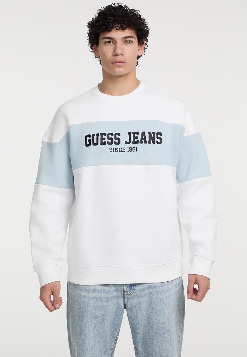 Felpa bianca con dettagli azzurri chiari, caratterizzata dalla scritta "GUESS JEANS" stampata in bold nero. Tessuto morbido e design dalla vestibilità comoda.