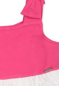 Top de algodón rosa con un detalle de lazo en el hombro y un bajo blanco con volante. Incluye un acento de logotipo en hardware plateado.