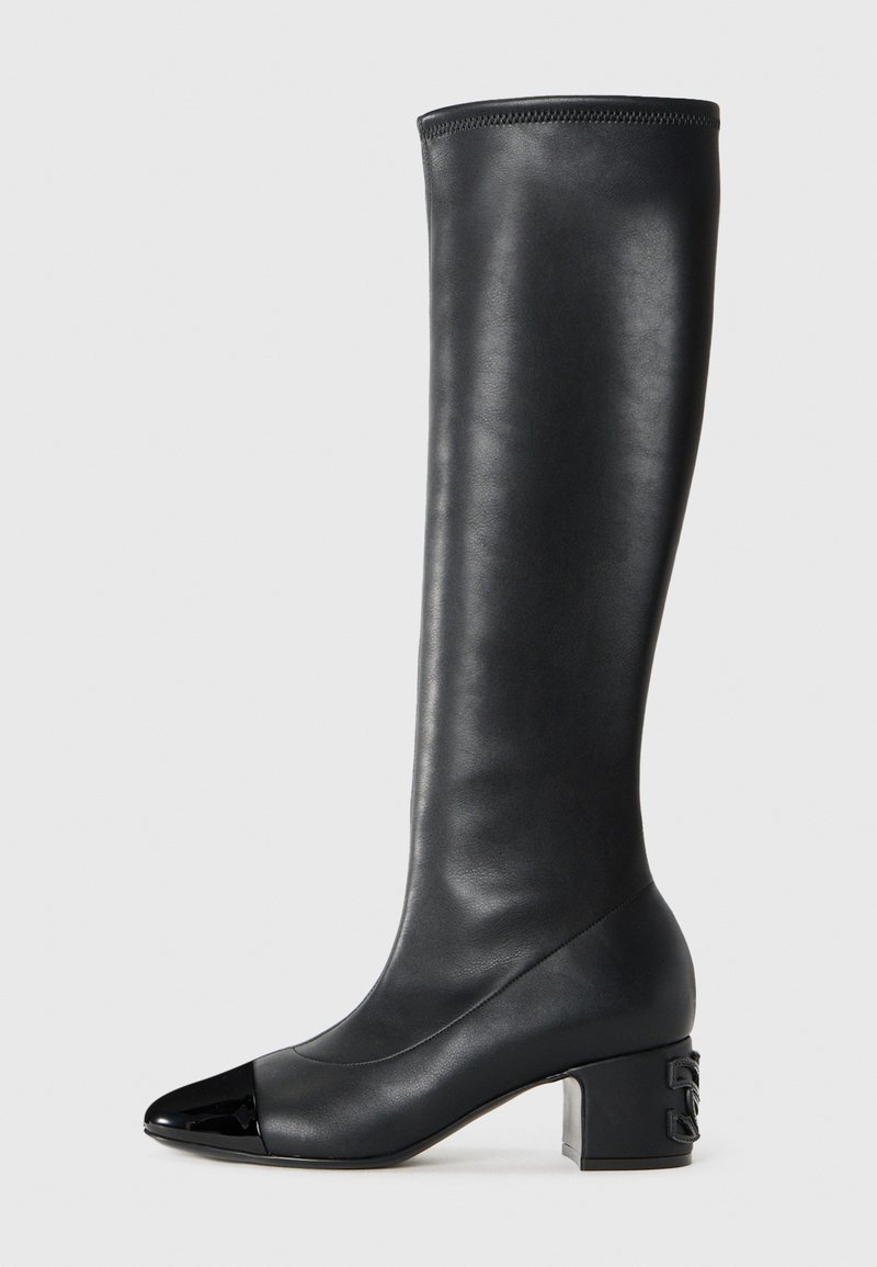 Bota alta de cuero negro con puntera brillante en negro, tacón cuadrado y detalle del logo en el talón, mostrada contra un fondo claro y liso.