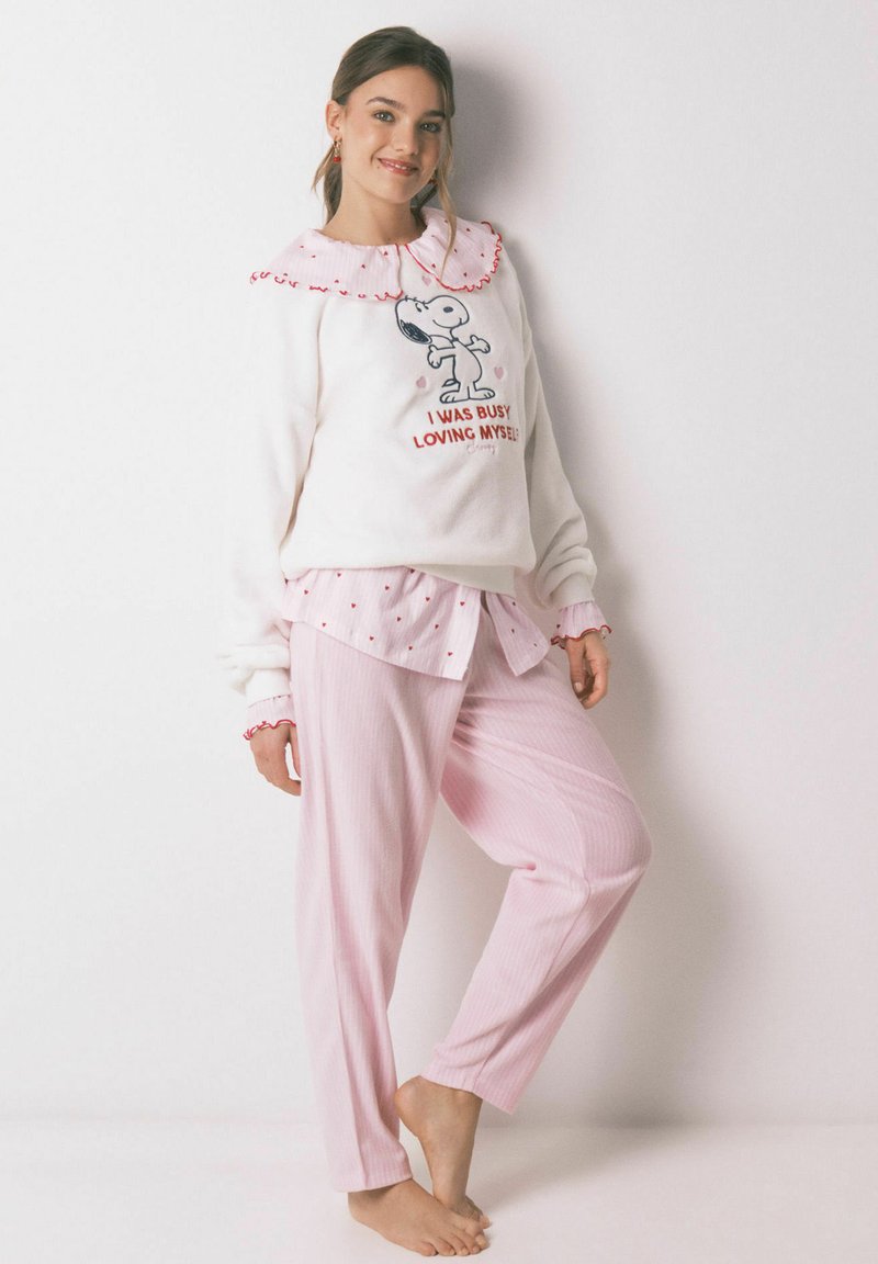 Biała bluza polarowa z czerwonym falbankowym kołnierzem i grafiką Snoopiego. Jasnoróżowe spodnie piżamowe w paski. Pod spodem koszula w kropki na guziki.