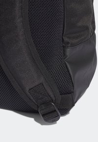 Black backpack featuring a textured mesh side panel, smooth fabric accents, and a plastic buckle on a webbed strap for secure fastening.