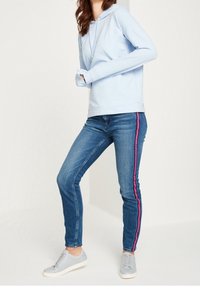 Sudadera azul claro con cordón, combinada con vaqueros azules con rayas laterales rosas y zapatillas grises. Atuendo sencillo y casual.