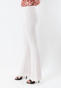 Pantaloni a vita alta, color crema, a zampa d'elefante con chiusura a zip sul retro, tessuto testurizzato, abbinati a sandali neri con tacco alto.