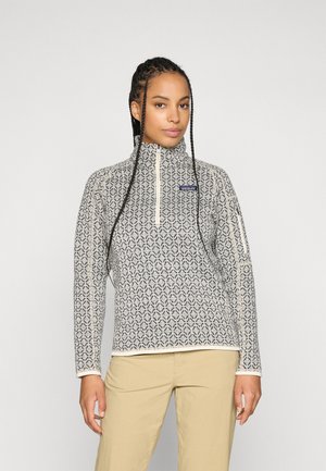 Fleece megztinis su geometriniu juodai baltu raštu, aukštu apykaklė, ilgomis rankovėmis ir priekiniais užtrauktukais. Oda su grietinėlės spalvos akcentais.