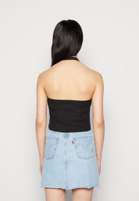 Top cropped preto com alças, combinado com uma saia mini de ganga azul clara com bainha desfiada e bolsos traseiros. Design simples e ajustado.
