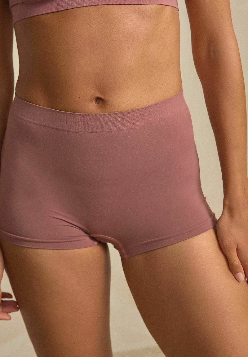 Kvinde iført mauve højlivet sømløst boyshort undertøj og matchende bralette, der viser maven og de øverste lår.