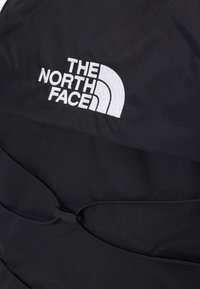 Schwarzer Rucksack mit strukturierter Oberfläche, auf dem sich das auffällige, weiße gestickte Logo von "The North Face" sowie ein sicheres Verschlussmechanismus befinden.