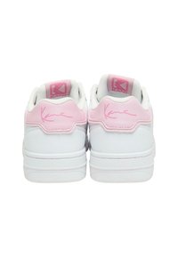 White sneakers with pink accents, featuring a smooth leather texture and a signature detail on the heel. Rounded, cushioned collar design.