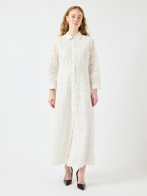Robe blanche à manches longues avec un col, ornée de motifs brodés en œillets. Le tissu est léger et texturé.