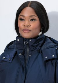 Chaqueta acolchada navy con cuello alto, broches de plata, un toque metálico y una textura suave y brillante.