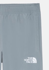Svetlo sivi atletski hlače z elastičnim pasom, stransko žepom in belim logotipom "The North Face" na spodnjem levem delu.