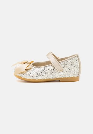 Børns glitrende sølv balletsko med beige sløjfe og rem samt lys brun sål, vist fra siden på hvid baggrund.