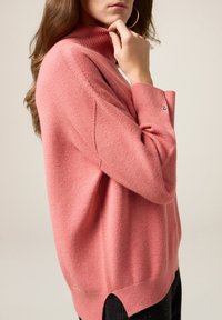 Maglioncino rosa a collo alto in morbido tessuto lavorato a maglia, con colletto a costine, spacchi laterali sull'orlo e dettaglio con bottoni sulle maniche.