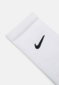 Chaussettes Nike blanches avec une texture côtelée, présentant un logo swoosh brodé noir sur le côté. Le revers est doux et flexible.