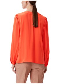 Langärmlige Bluse aus leuchtend orangefarbenem Stoff, mit glatter Textur, breiten Manschetten und lockerer Passform. Die Rückansicht zeigt ein schlichtes Ausschnittdesign.