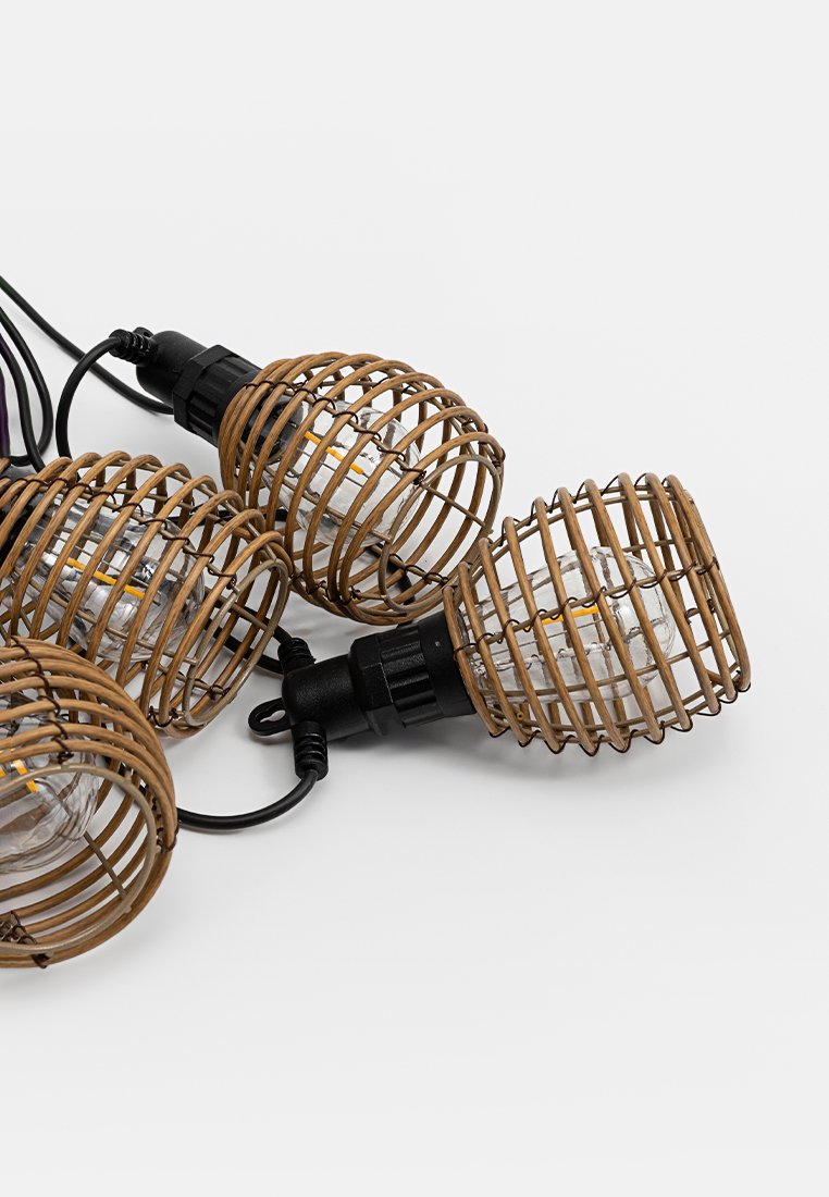 Szereg czterech lamp wiszących z plecionymi, brązowymi abażurami z rattanu, przezroczystymi żarówkami, czarnym okablowaniem i matowym wykończeniem.