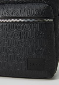 Čierny textúrovaný batoh s embosovaným logom "HUGO", so strieborným zipsom a obdĺžnikovou nášivkou s logom.