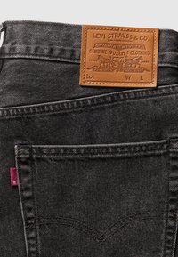 Poche arrière d'un jean en denim noir avec un patch en cuir beige Levi Strauss & Co. et une petite étiquette en tissu rouge sur la couture latérale.
