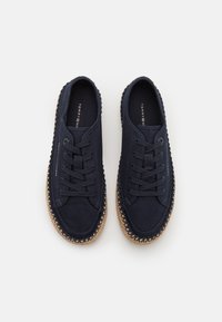 Marinblå canvas-skor med rund tå, snördesign och en texturerad espadrille-sula med vävd detaljer längs kanten.