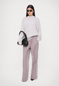 Jasnofioletowy, oversize sweter, luźne malwowe spodnie z bocznymi akcentami oraz czarna, teksturowana torebka; eleganckie czarne okulary przeciwsłoneczne.