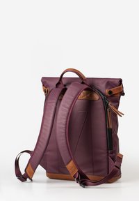 Zaino a cilindro bordeaux con accenti in pelle marrone, spallacci imbottiti, tasca con zip e manico superiore per il trasporto. Texture liscia.