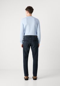 Ανοιχτό μπλε μπλούζα με μακριά μανίκια και σκούρα τζιν, με εφαρμοστή σχεδίαση, πίσω τσέπες, και καφέ υποδήματα, ορατή από πίσω.