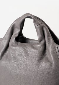 Weiches graues, genarbtes Lederhandtasche mit integriertem Schlaufengriff und dezentem, geprägtem Logo "aunts & uncles" auf der Vorderseite.