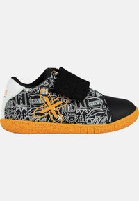 Zapatilla en blanco y negro con patrones gráficos, suela de goma naranja y correa de velcro negra. Tiene una punta redondeada y material texturizado.