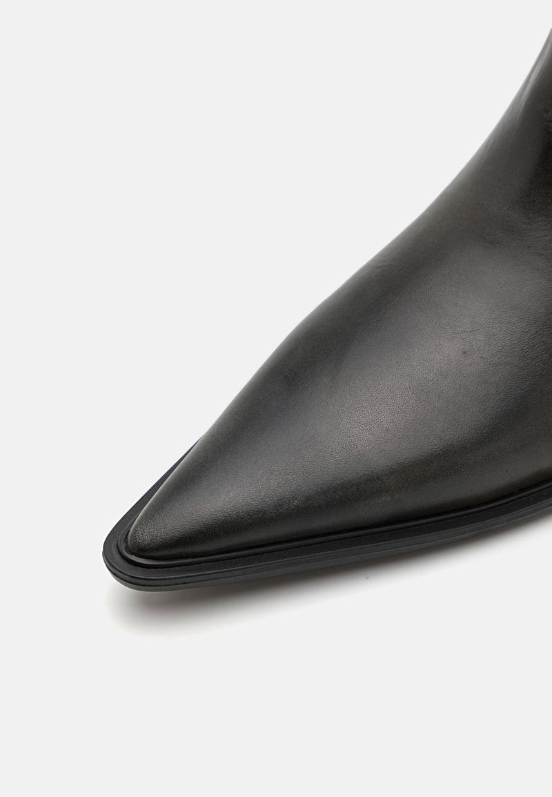 Bota de tacón alto de cuero negro con punta afilada, textura suave y silueta esbelta. Presenta un diseño minimalista y un perfil elegante.
