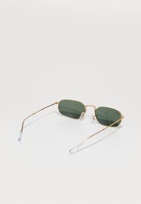Gafas de sol de metal dorado con lentes tintados en verde, de forma octagonal, con brazos delgados y acentos transparentes en las patillas. Diseño sencillo y moderno.