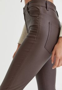 Pantalon marron moulant en matière lisse. Caractérisé par une taille haute, deux poches arrière, et un design épuré avec des coutures minimalistes.