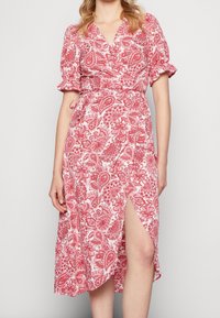 Robe portefeuille à imprimé cachemire rouge et blanc, longueur mi-mollet avec manches courtes bouffantes, décolleté en V et fente latérale. Tissu doux avec un design fluide.