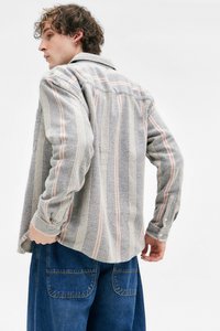 Gråstripet skjorte med rosa og hvite striper, strukturert stoff, knappe mansjetter, stukket inn i blå denimbukser. Modellen vist bakfra.