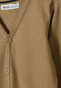 Beige gestrickte Strickjacke mit V-Ausschnitt, ausgestattet mit zwei Knöpfen und feiner Textur. Etikett liest "minoti". Weiches, leichtes Material.