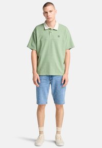 Grön polo tröja med vit krage, ihop med blå denim shorts. Modellen har på sig krämfärgade sneakers och randiga strumpor.