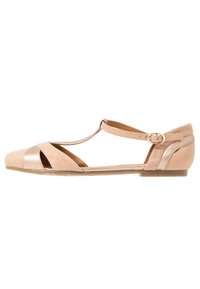 Sandalia plana beige con tiras en T, hebilla dorada, lados recortados y materiales de cuero y ante combinados.