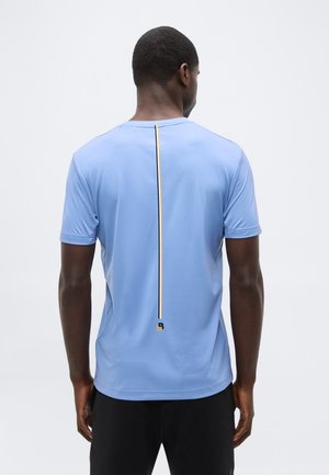 Mees, kellel on seljal vertikaalne musta ja kollase triibuga helesinine lühikeste varrukatega särk, kombineeritud mustade pükstega.