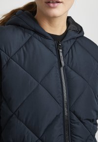 Navy quilted puffer vest with a hood, featuring a front zipper and ribbed collar. The fabric has a smooth, matte finish.