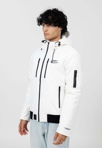 Giacca bianca con zip e dettagli neri, presenta un cappuccio, molteplici tasche con zip e un cinturino nero a costine. Il tessuto ha una consistenza liscia.