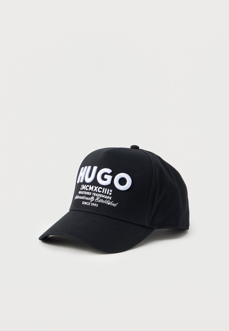 Cappellino da baseball nero con il testo ricamato bianco "HUGO" e "Dal 1993" sul pannello frontale, esposto su uno sfondo chiaro e semplice.