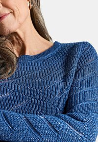 Blauer gestrickter Pullover mit strukturiertem Muster, diagonalen Linien und leichtem Schimmer. Rundhalsausschnitt und lange Ärmel.