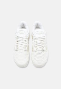 Baltas sporta kurpes ar teksturētu augšdaļu, izteiktām shoelace un polsterētu apkakli. Zoles dizainā ir redzams medus kāruma raksts.