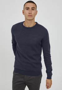 Marineblauem Strickpullover mit Rundhalsausschnitt und langen Ärmeln. Glatte Textur mit gerippten Bündchen und Saum. Slim Fit mit subtiler Markenetikette.