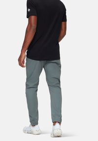 Zwarte t-shirt met korte mouwen met een logo op de linkerschouder, gecombineerd met lichtgrijze slim-fit broek en witte sportschoenen.
