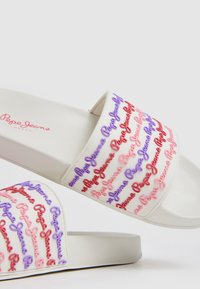 Infradito bianche con un design della logo rialzato in rosa e viola. Realizzate in materiale liscio con suola piatta e punta aperta.