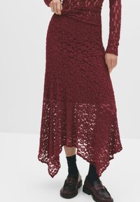 Burgunderfarbene Spitzenrock mit gewelltem Saum und strukturiertem Blumenmuster. Kombiniert mit schwarzen Mokassins und marineblauen Socken, mit einem eng anliegenden Bund.