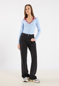 Lys blå langermet topp med dyp V-hals og maroon stripete krage, kombinert med høy midje svarte vide bukser og joggesko.