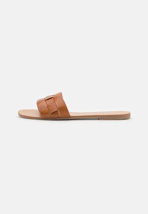 Sandale en cuir marron avec deux larges sangles dotées d'un détail de boucle, semelle plate et texture lisse. Design minimaliste, style décontracté.